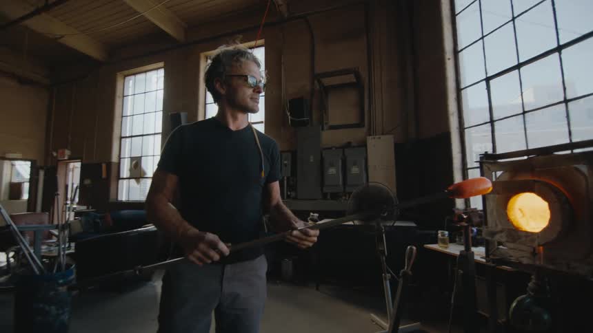A glass blower spinning a new piece in electric oven beginning a new work of art
