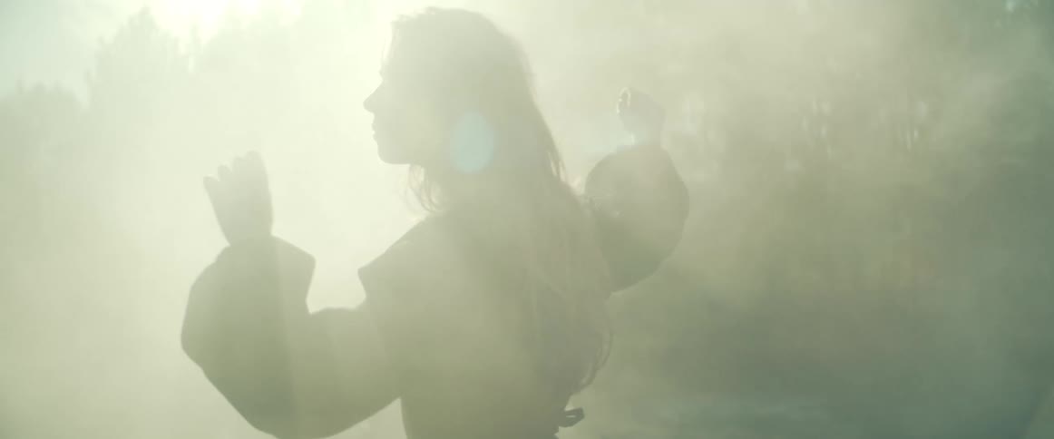 A woman is dancing outdoors in a wooded area with fog