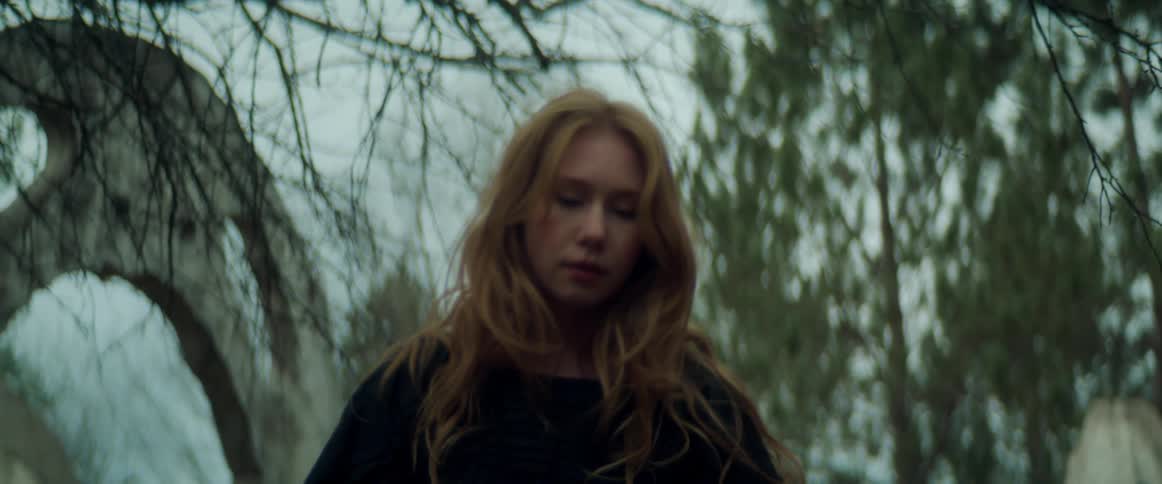 A teenage girl wearing black is outside dancing near trees