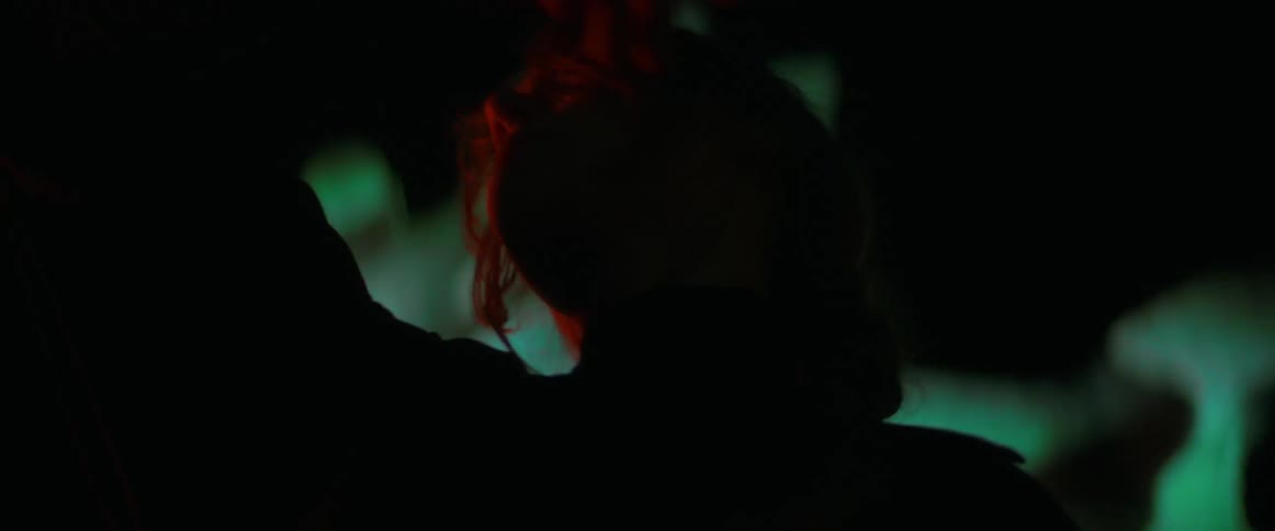 Blonde woman wearing black clothes dance in front of an outdoors projection at night