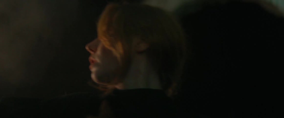 Blonde woman wearing black clothes dances in front of an outdoors sculpture at night
