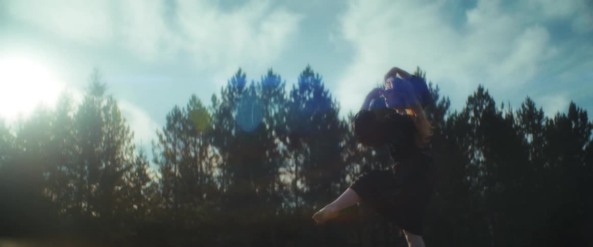 Young woman holding a dance pose in front of the tree line at sunset