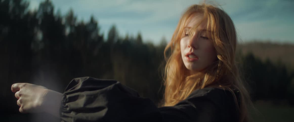 Woman with wavy red hair and black dress dances in the forest