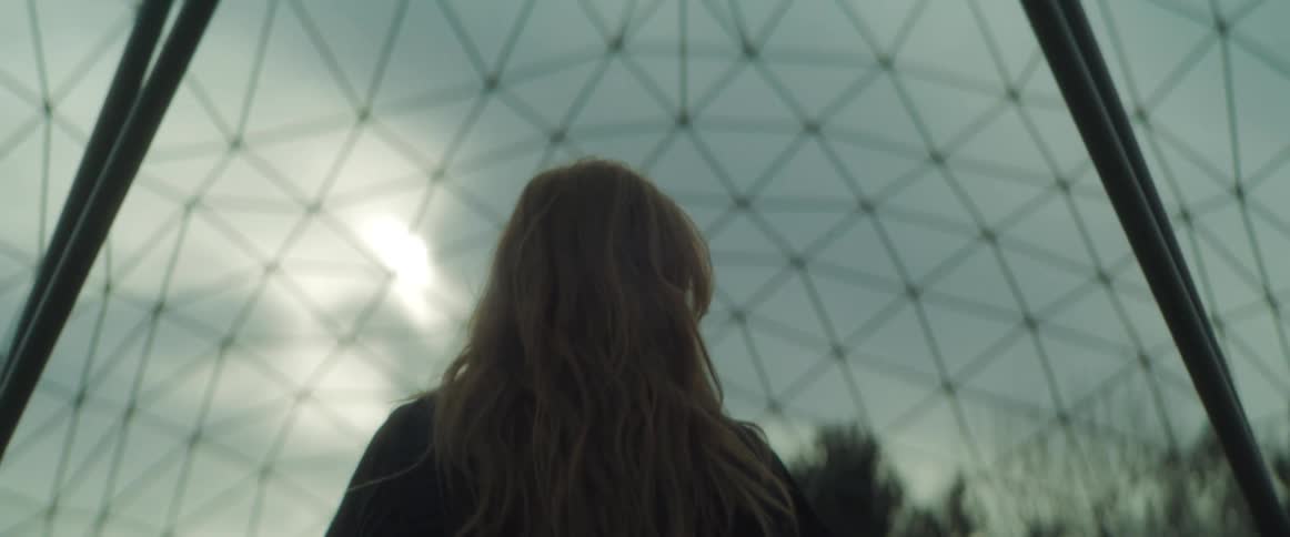 Woman walks through enclosure of multiple interconnecting struts under and overcast sky
