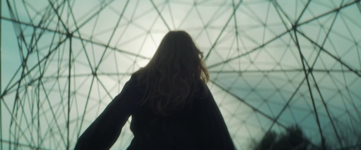 Woman walks in to large structure made of interconnected struts