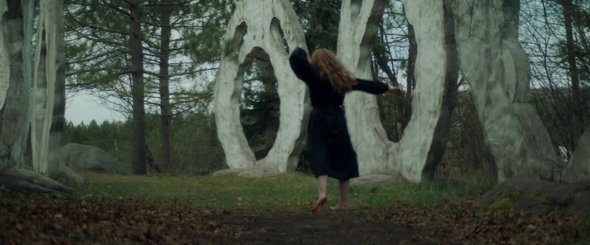A woman is dancing in front of odd sculptures
