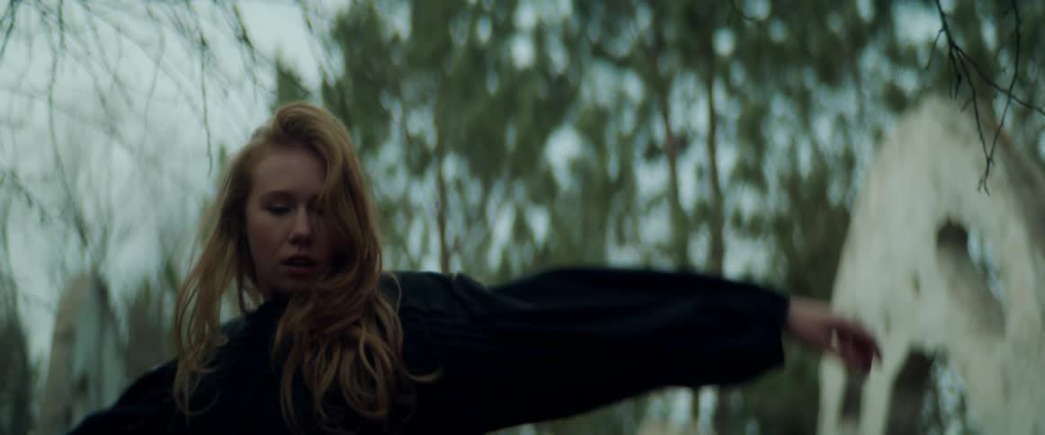 Blonde woman wearing black clothes dance in front of an outdoors sculpture at daytime