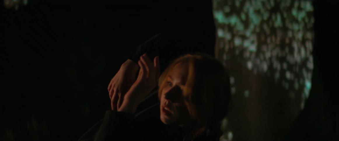 Blonde woman wearing black clothes dance in front of an outdoors projection at night