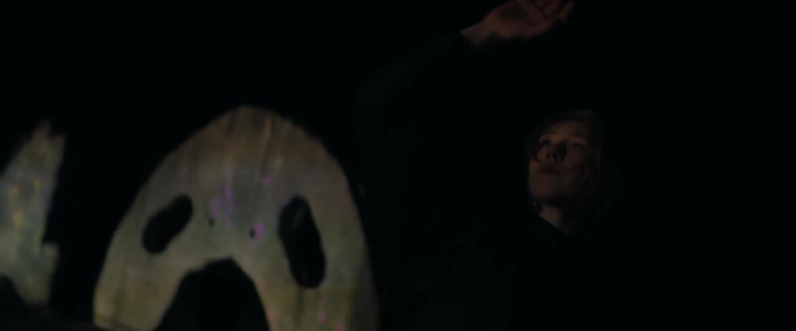 A woman dances outdoors in front of iridescent sculptures at night