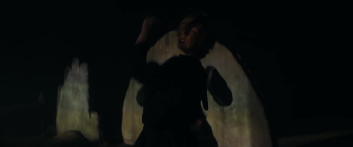 Blonde woman wearing black clothes dance in front of an outdoors sculpture at night