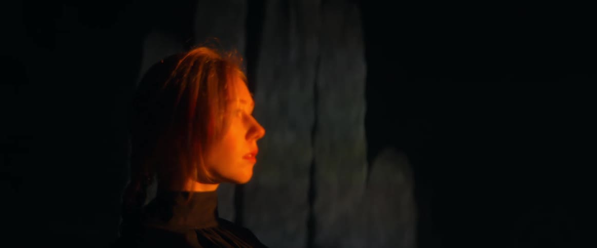 Young blonde woman laying on the ground near outdoor sculptures at night