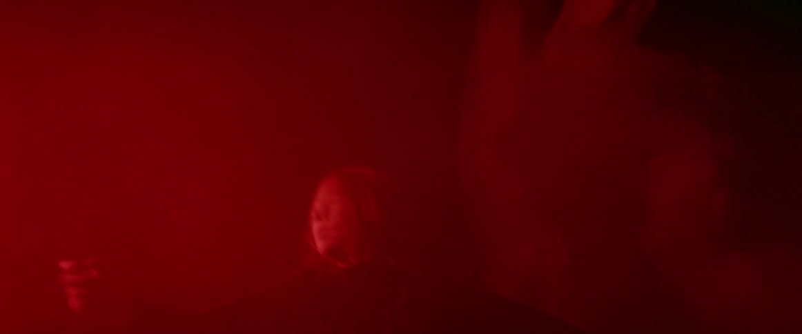 A woman dancing on a set with projected light shining behind her and smoke billowing around her