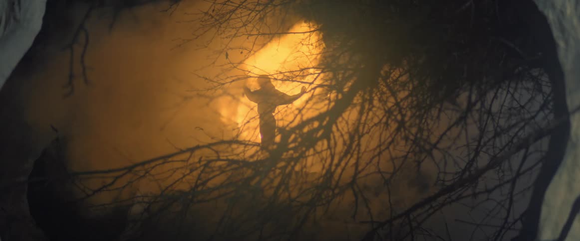 A woman dances in front of a fire in a forest