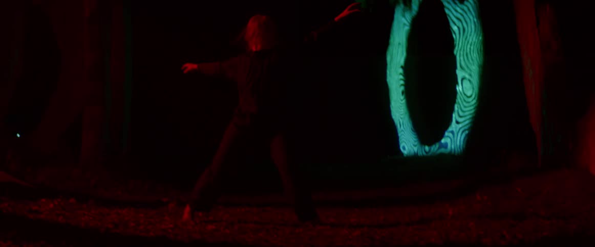 Blonde woman wearing black clothes dance in front of an outdoors projection at night