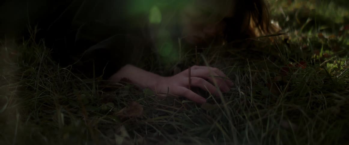 A woman lying in the grass slowly sits up looking anxious