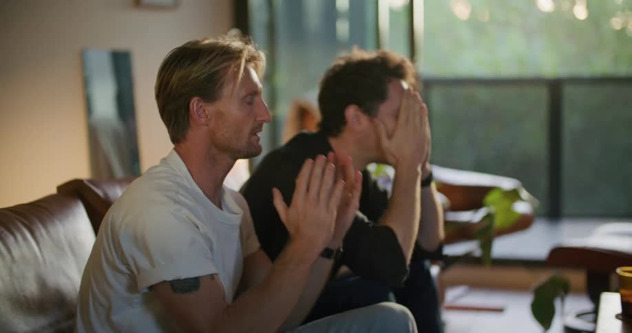 Two men are watching television and look upset