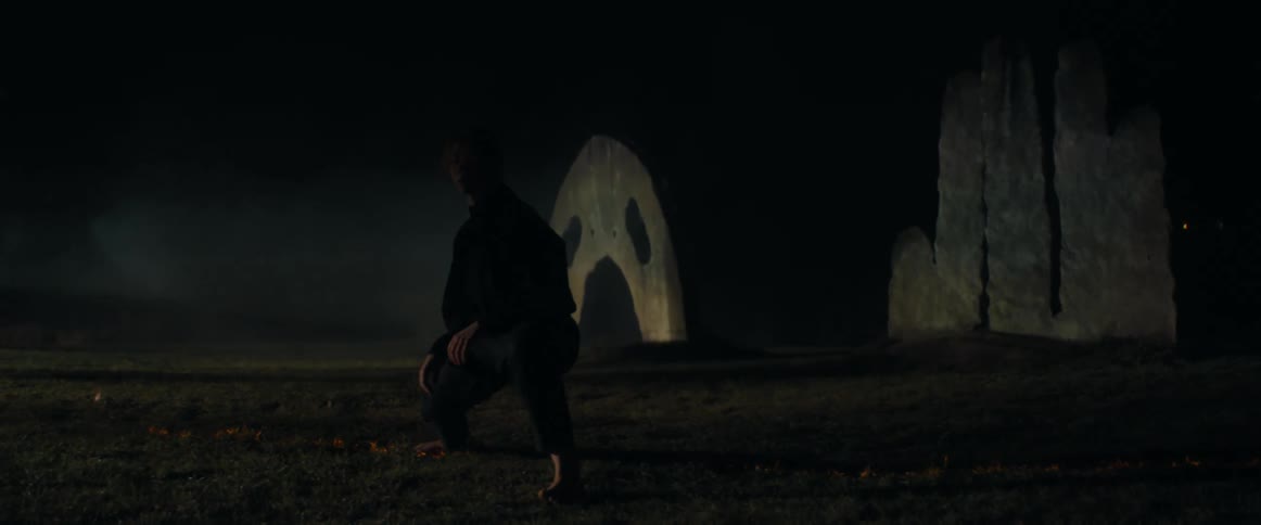 Blonde woman wearing black clothes dances in front of an outdoors sculpture at night