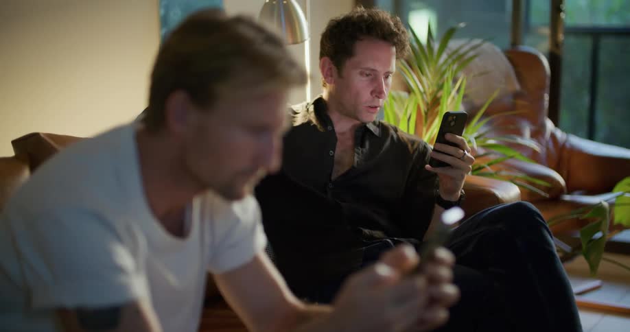 Two friends are looking at their cell phones and sitting together