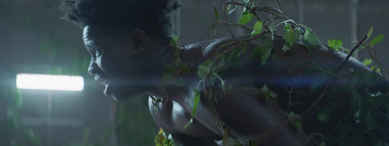 Man with branches and leaves on his back pants and breathes heavily as he bends over
