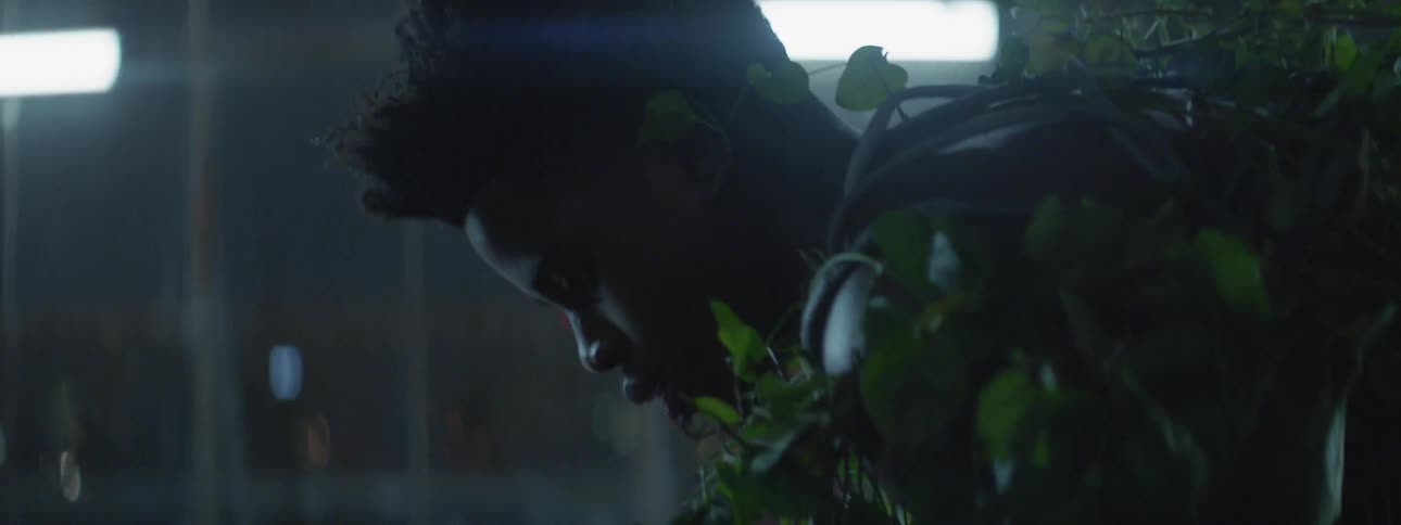 A man covered with vines is bending forward at night