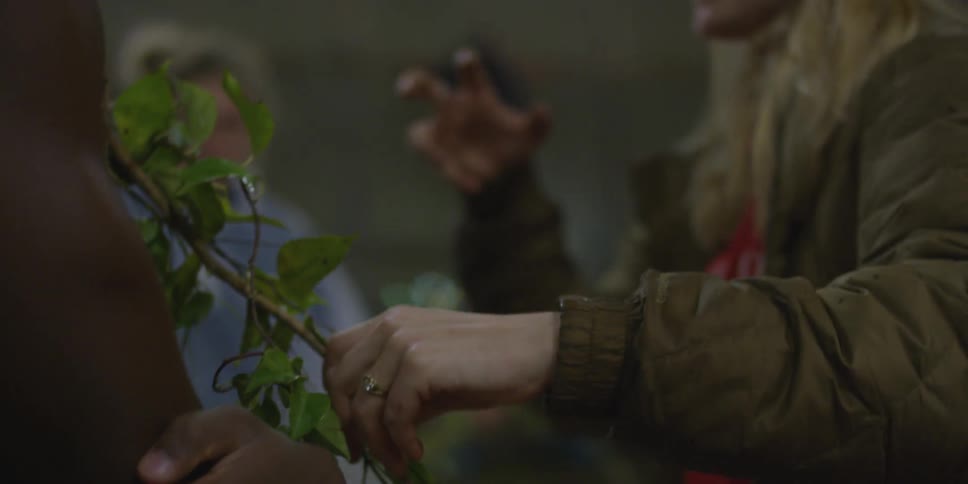 A woman talks with someone while holding onto vines on him