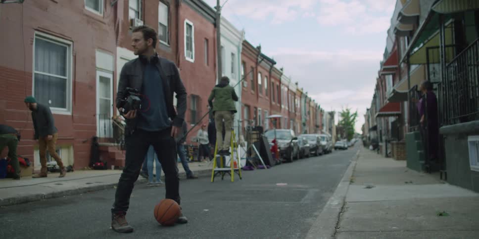 Director kicking a basketball while film crew preps for a shot in the background