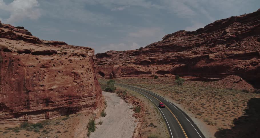 A red truck travels on a road through the desert badlands with mountains and mesa on the roadsides