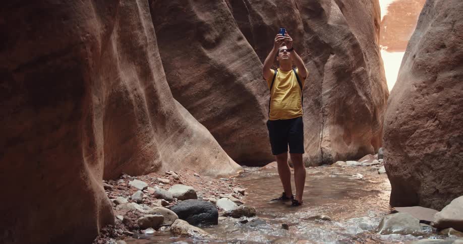 A man standing at the base of a narrow gorge uses his phone to take photographs