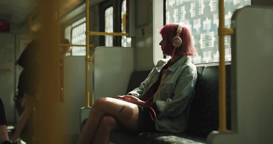 A teenage girl is sitting in a seat on a train with headphones on her head
