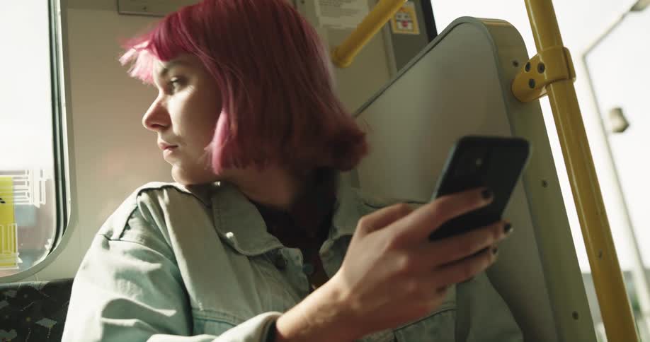 A young woman sits on a city bus looking at her cell phone