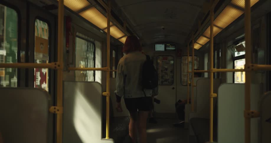 A teenage girl with a backpack on her shoulder walks on to a train and sits down
