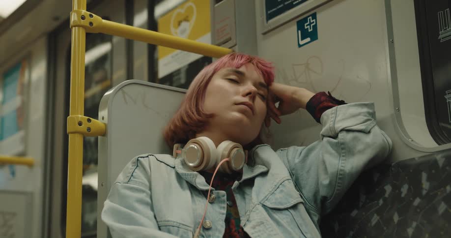 A young woman dozing off on a subway readjusts her seating position
