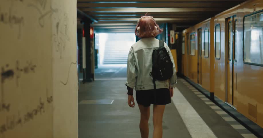 A woman wearing headphones walks through a subway station during the day