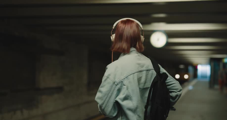 A woman stands to wait for a subway and looks at her cell phone