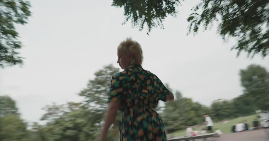 A young woman runs to a park bench and begins to dance on top of it
