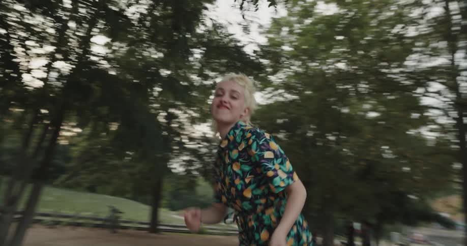 A young woman dances while standing atop a bench in a public park on a cloudy day