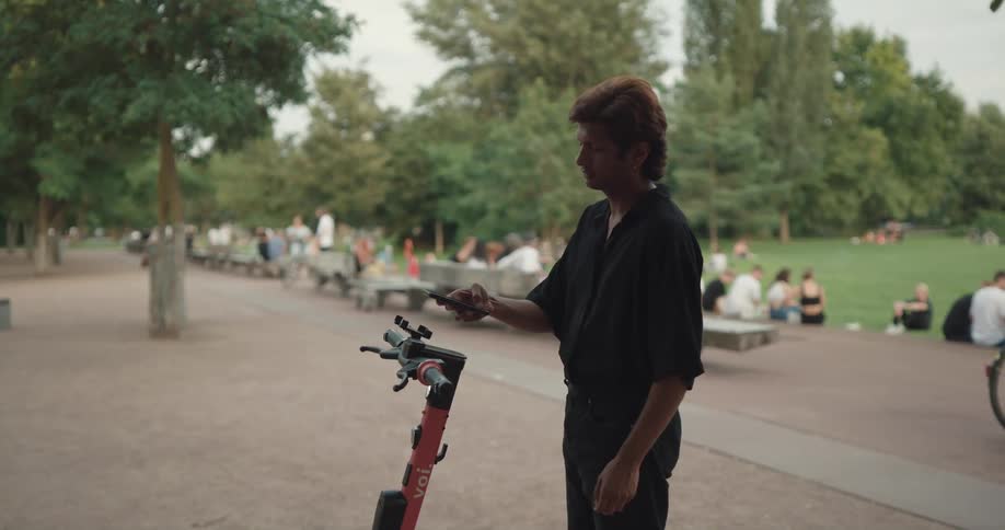 A man uses his smartphone to rent an electric scooter in a park