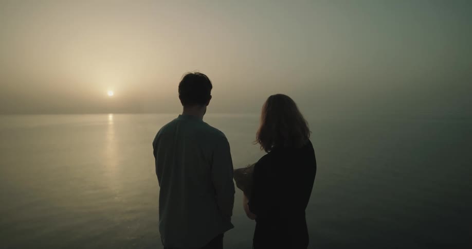 Man and woman stand on shore on foggy day spreading funerary ashes onto the water