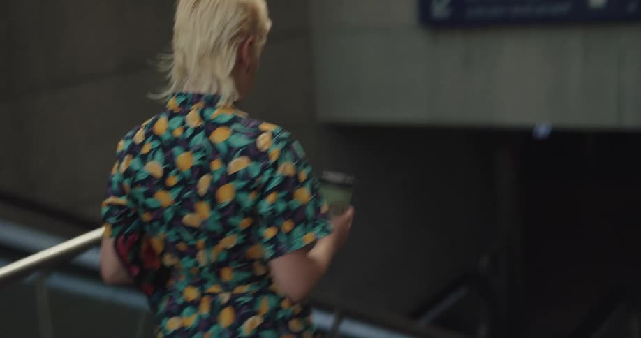 A woman descends a staircase into a subway while carrying a disposable coffee cup