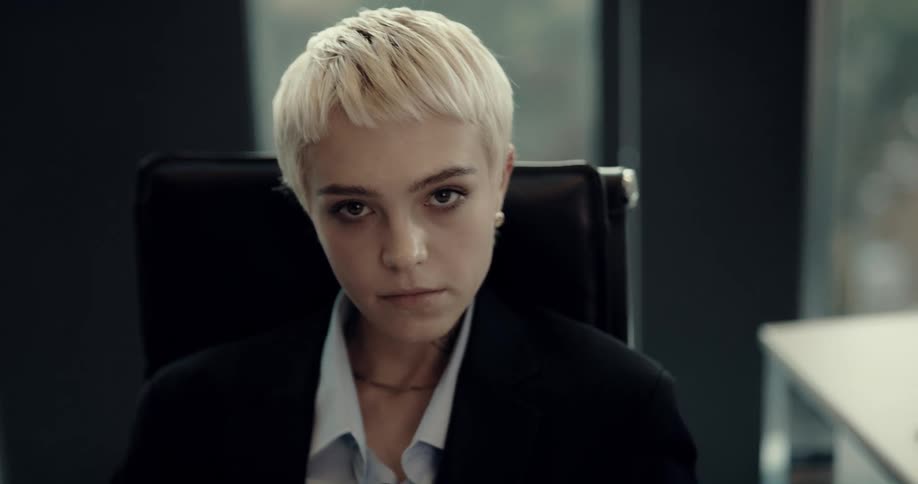 Businesswoman with short hair black blazer jacket and blue shirt sits at desk in the office