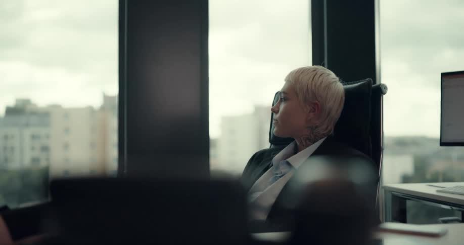 A woman reading a paper while sitting at a desk in an office places the paper on her desk and takes a sip from her coffee cup