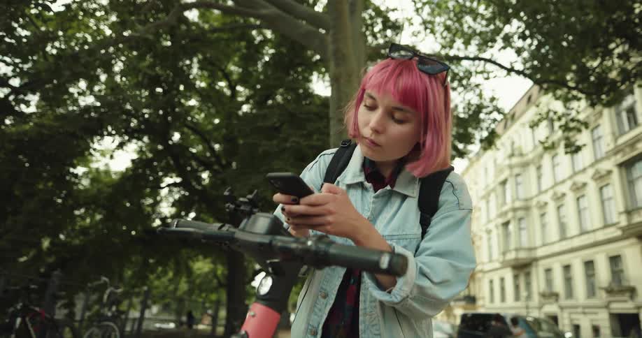A woman is using her cell phone to activate an electric scooter in a city