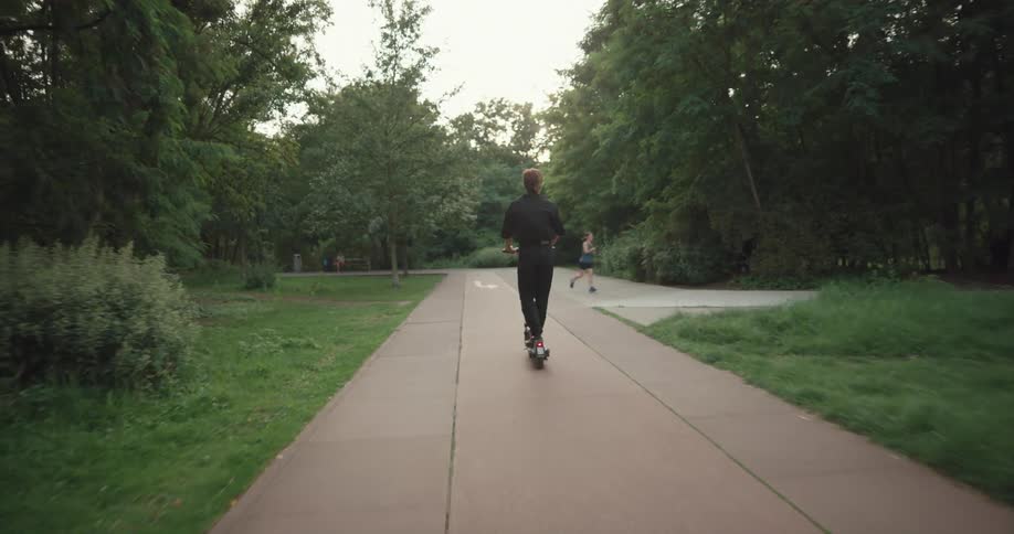 A person rides an electric scooter on a park sidewalk