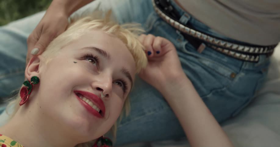 Young happy short haired blonde woman reclined on the lap of her partner on a park