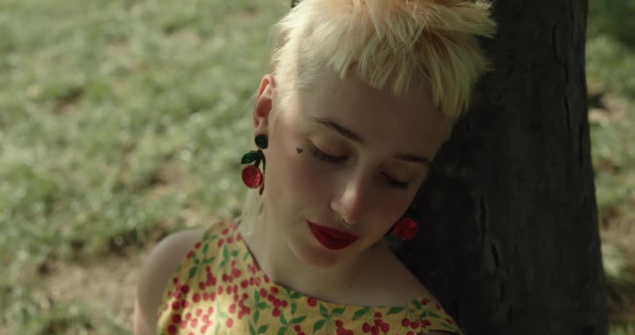 A young woman sleeping against a tree suddenly raises her head to smile into the camera