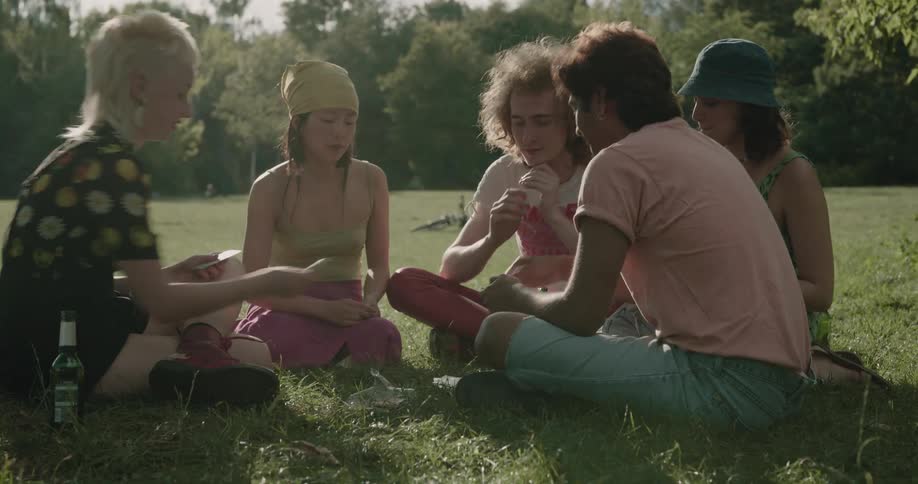 Group of friends playing cards sitting over the green grass on a park