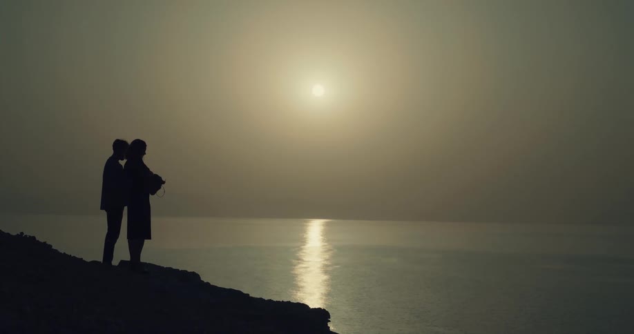 Silhouette of a couple holding an urn spreading ashes of a loved one into the ocean at sunset