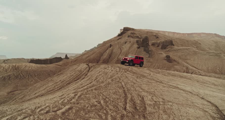 Aerial of red jeep wrangler off roading on hills in the desert