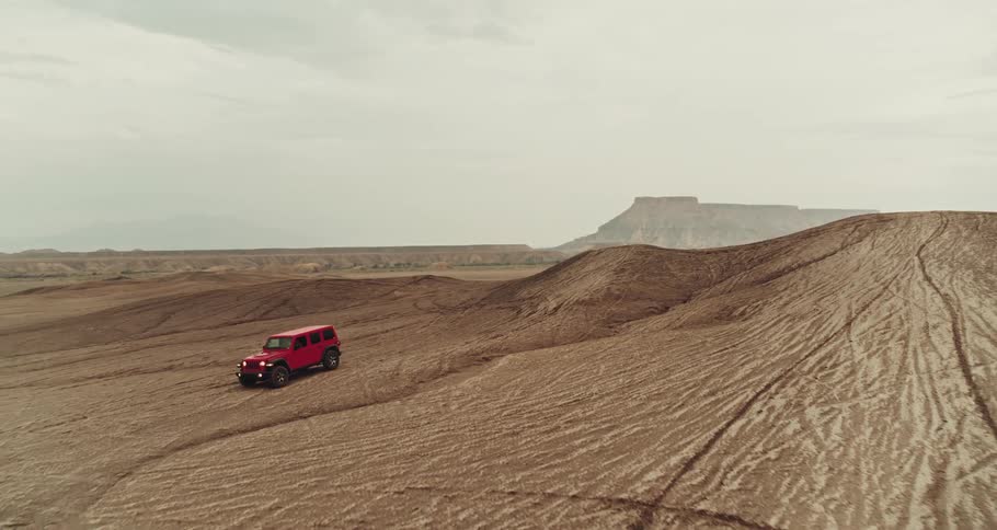 A vehicle travels offroad across rugged terrain in an arid wilderness on a cloudy day