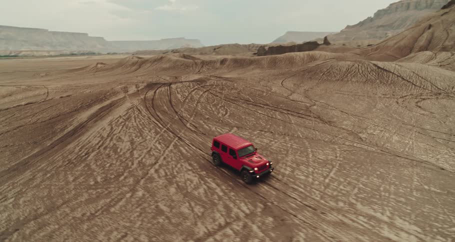 A red truck travels across the desert with mountains and mesa in the distance
